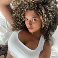 Emely Tuinder, Partnerin von Dortmund-Profi Ian Maatsen, liegt auf dem Bett in einem weißen Top und mit lockigen braunen Haaren